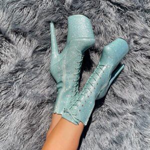 Groen blauwe paaldanshakken van Hella Heels aan de voeten van iemand, zittend op een grijs kleed